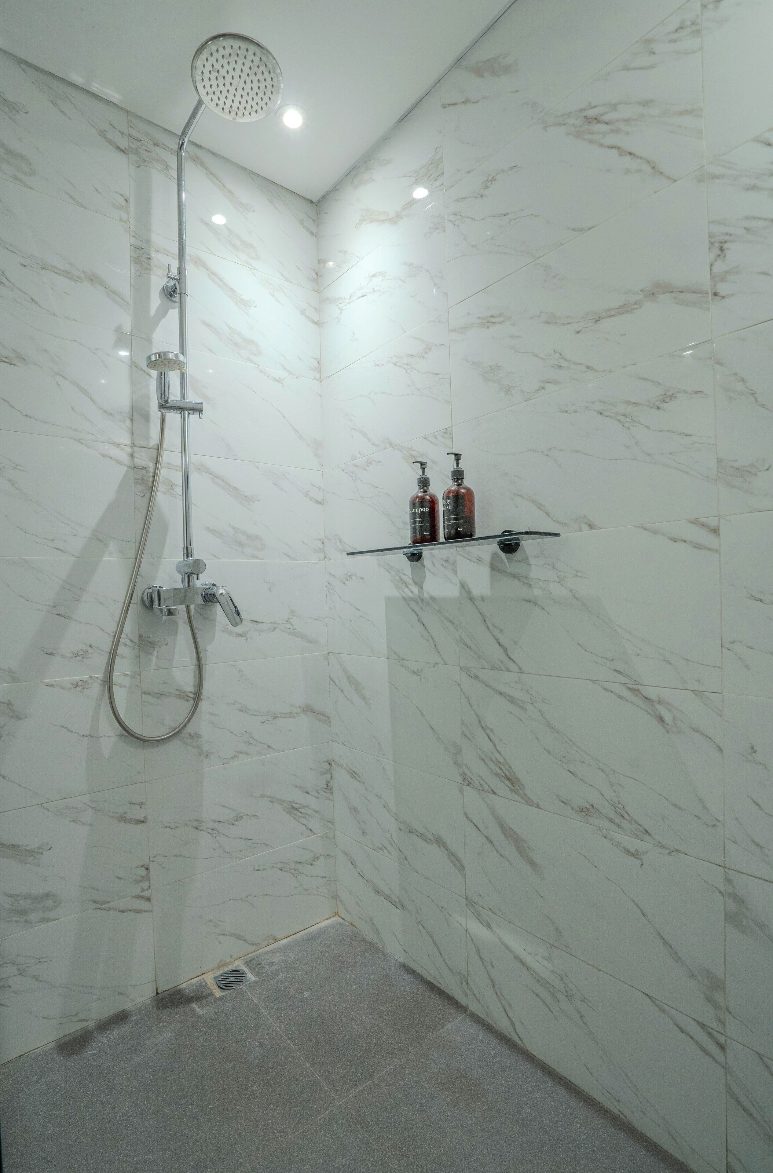 Un bagno con doccia, pareti in marmo e un ripiano con articoli da toilette.