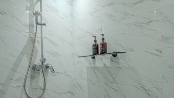 Un bagno con doccia, pareti in marmo e un ripiano con articoli da toilette.