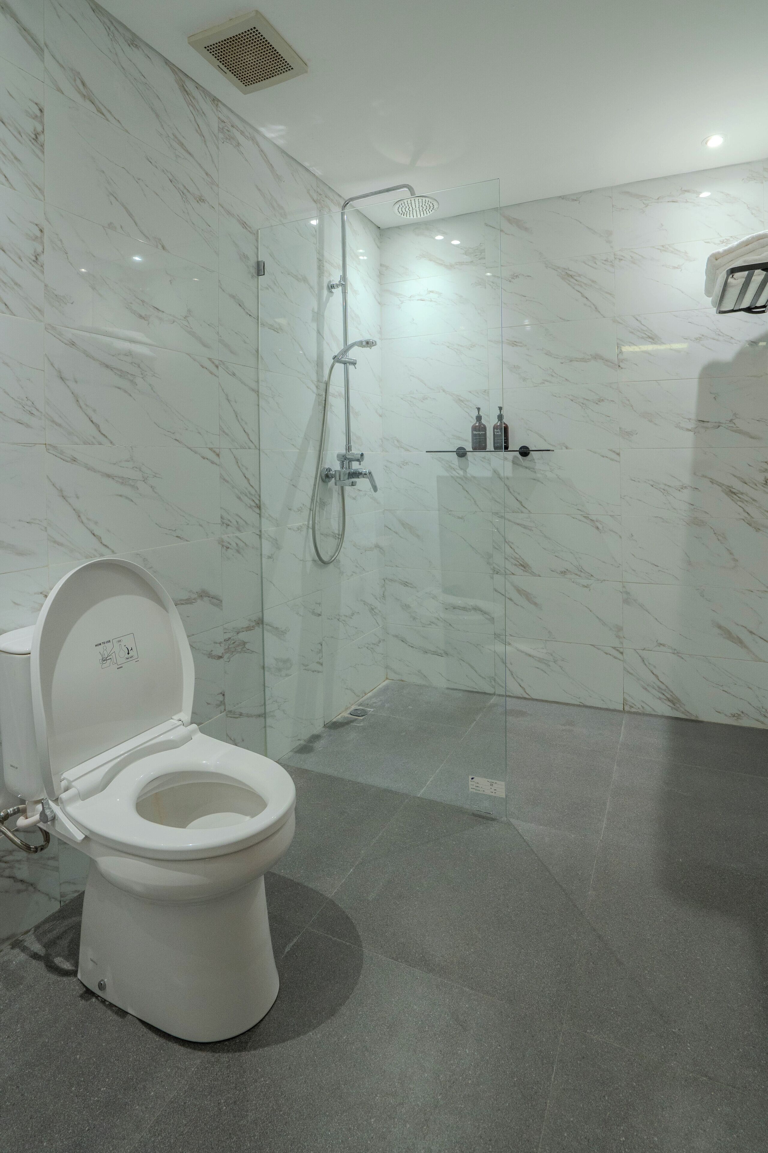 A modern bathroom with a toilet, a glass-enclosed shower, and a marble wall.