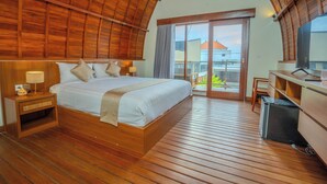 A spacious bedroom with a large bed, wooden flooring, a desk, and a sliding glass door leading to a balcony. - Villa Radha Pererenan (Pererenan)
