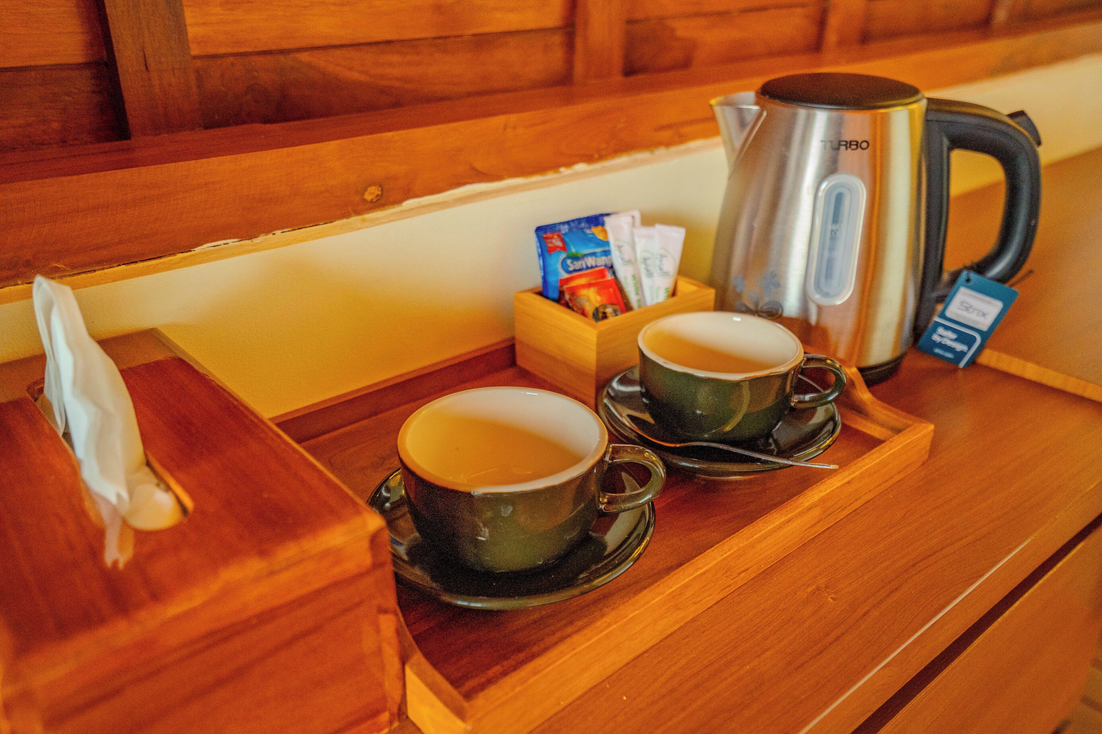 Una bandeja de madera con dos tazas de té, un hervidor y una caja de pañuelos.