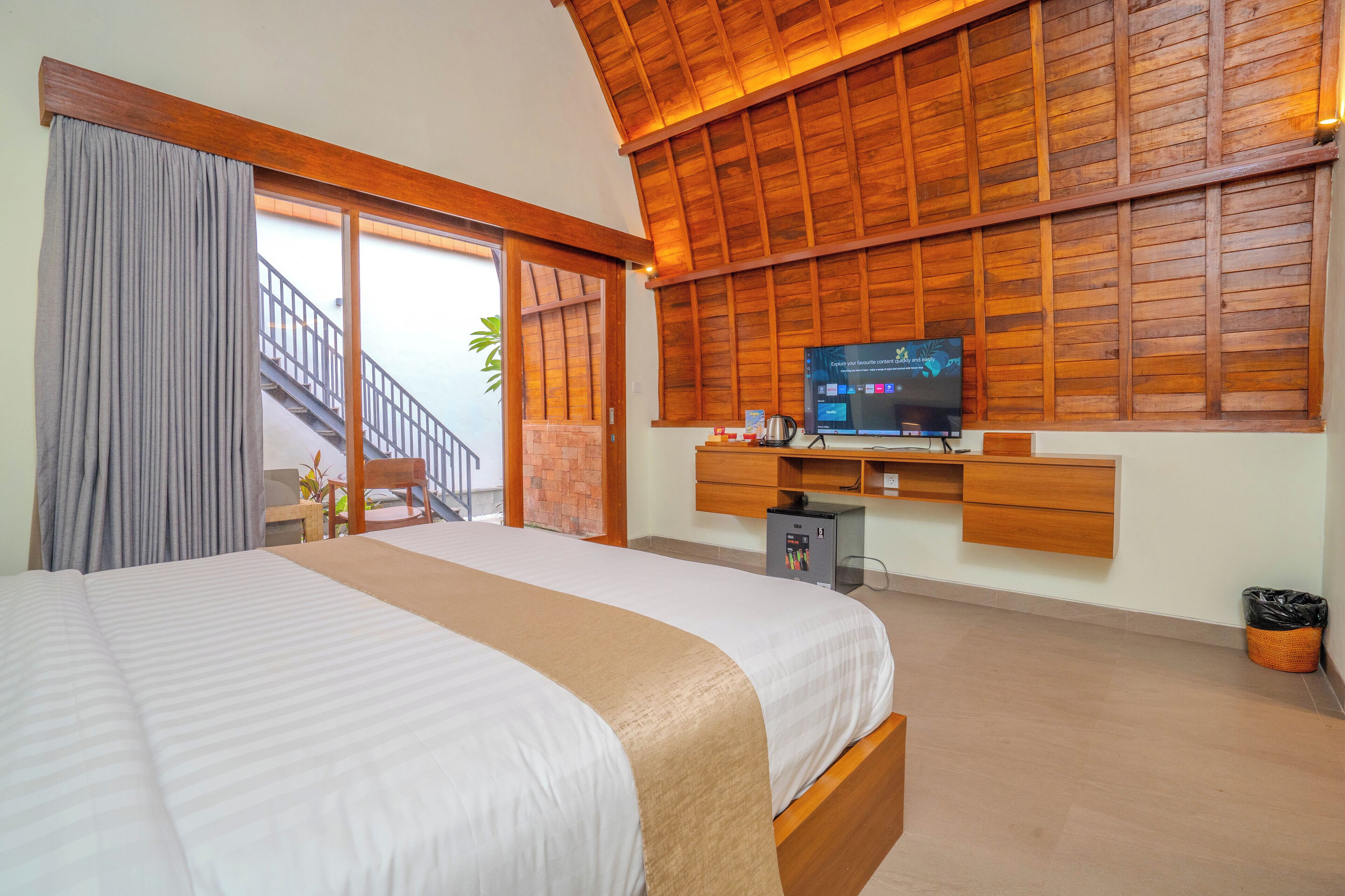 Une chambre avec un grand lit, un téléviseur fixé au mur et un escalier menant à un espace extérieur.