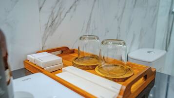 Una bandeja de madera con una caja blanca, dos recipientes de vidrio y un objeto rectangular blanco sobre una encimera de mármol.