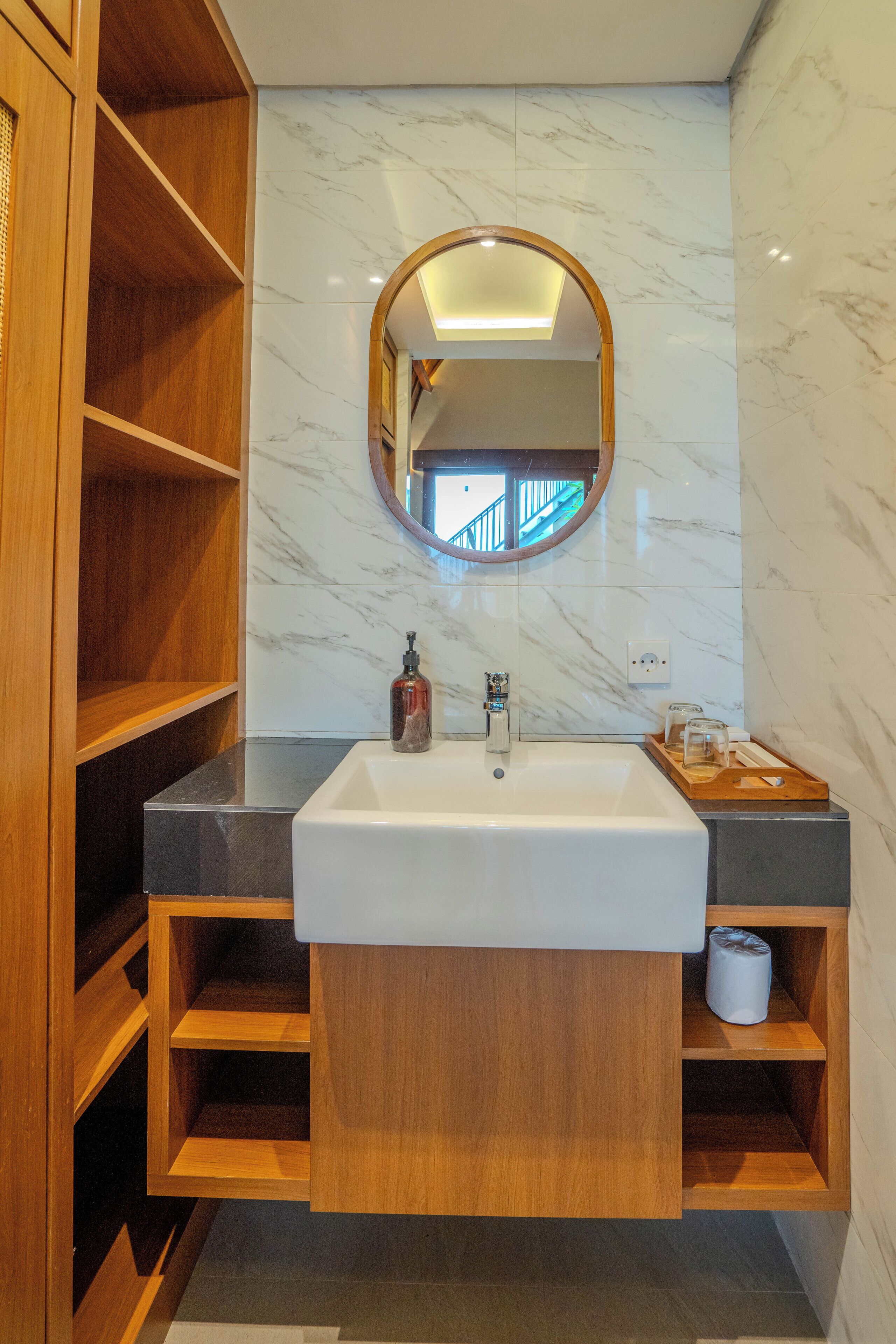 A bathroom with a marble wall, wooden shelves, a sink, and a mirror.