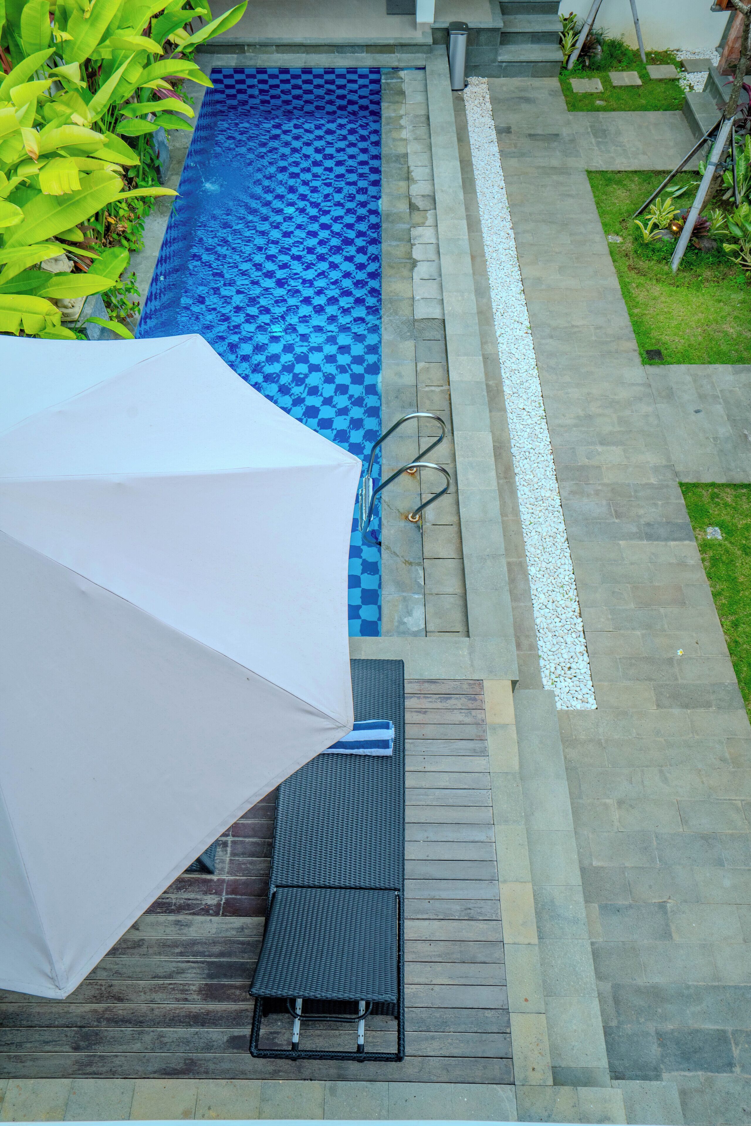 A swimming pool with a checkered pattern, a white umbrella, and a lounge chair.