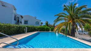 A swimming pool with a white building and palm trees in the background.