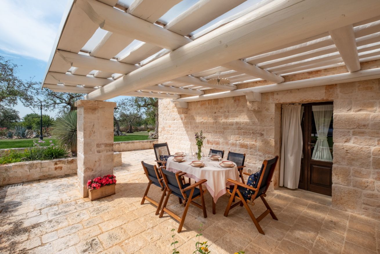 An outdoor patio with a stone wall, a pergola, and a table set for dining.