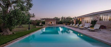 A swimming pool with lounge chairs, a stone building, and a tree.