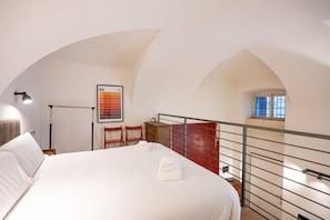 A hotel room with a large bed, a desk with a chair, a red railing, and a window.