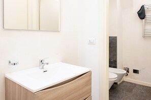 A modern bathroom with a white sink, wooden cabinet, and a toilet.