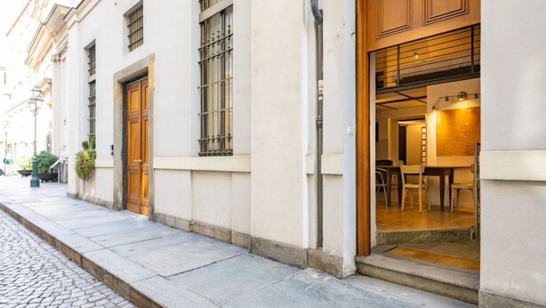 A building with a cobblestone street, large wooden doors, and a visible interior with a dining area. - Atriums Apartment Casa di Giulio (Torino)