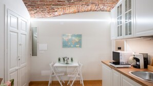 A compact kitchen with white cabinets, a microwave, a coffee maker, and a small dining table with chairs.