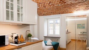 A compact kitchen with a brick ceiling, a bed with a green blanket, and a sliding glass door leading to a dining area.