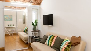 A living room with a sofa, a TV, a plant, and a mirror.