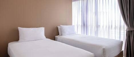 A hotel room with two beds, wooden flooring, a large window with curtains, and a ceiling with recessed lighting.