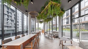A modern meeting room with long tables and chairs, large windows, and hanging greenery. - Salaya One Hotel & Service Apartment (Phutthamonthon)