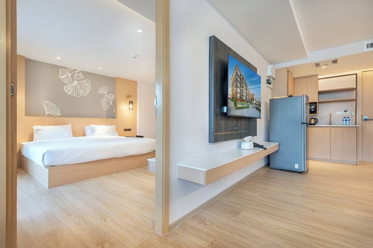Ein modernes Hotelzimmer mit einem großen Bett, einem integrierten Schreibtisch, einem Flachbildfernseher und einer Küchenzeile.