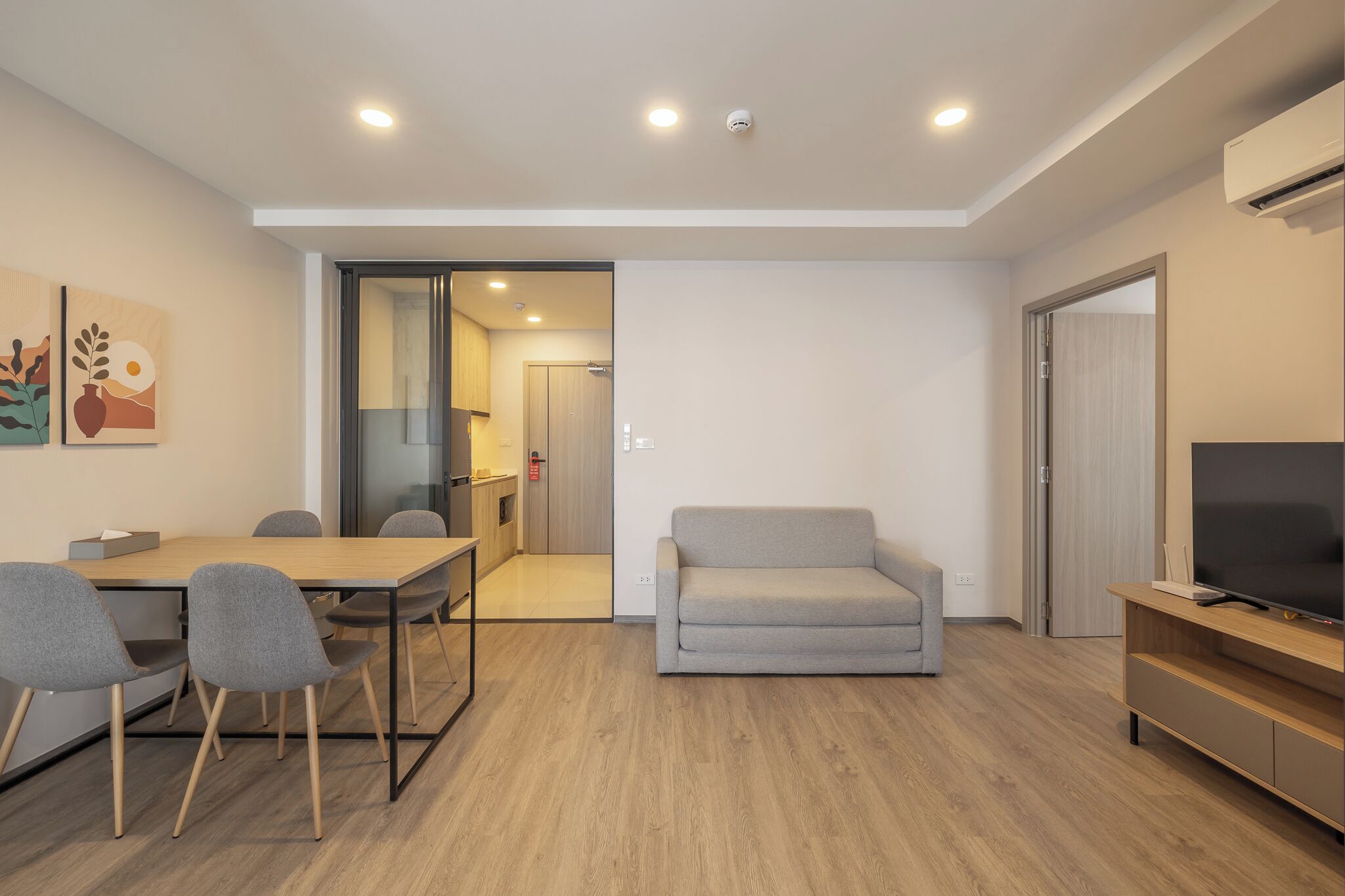 Una sala de estar moderna con un sofá, un televisor, una mesa de comedor con sillas y una cocina visible a través de una puerta abierta.
