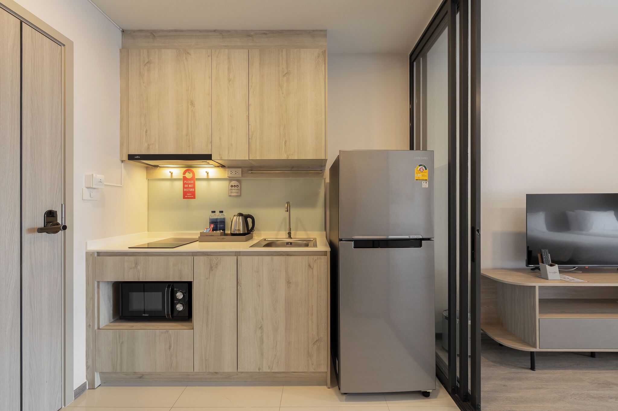 A compact kitchen with wooden cabinets, a built-in microwave, a stainless steel refrigerator, and a small sink.