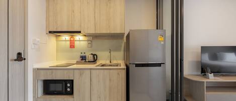 A compact kitchen with wooden cabinets, a built-in microwave, a stainless steel refrigerator, and a small sink.