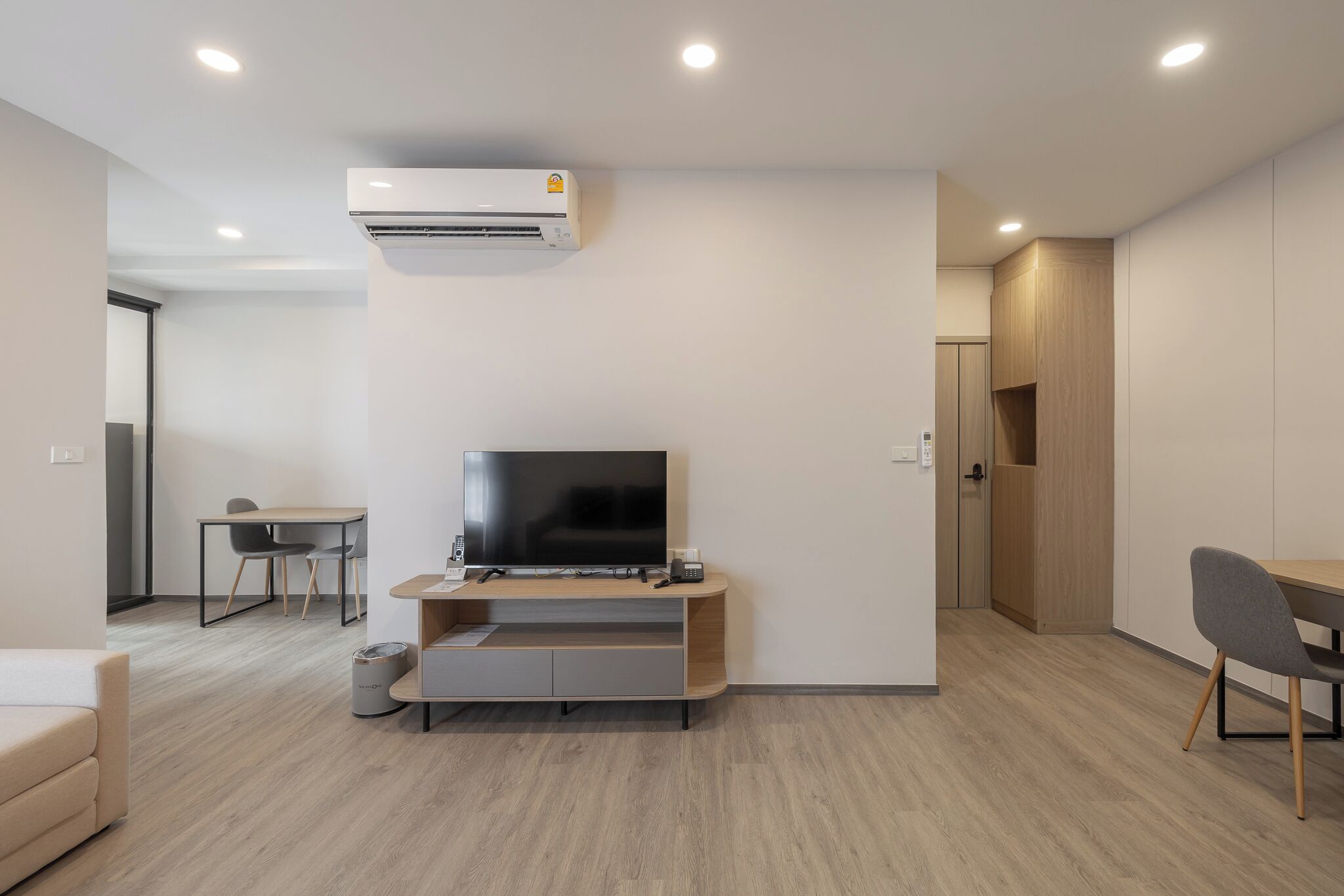 A modern living room with a flat-screen TV, wooden furniture, and built-in cabinets.