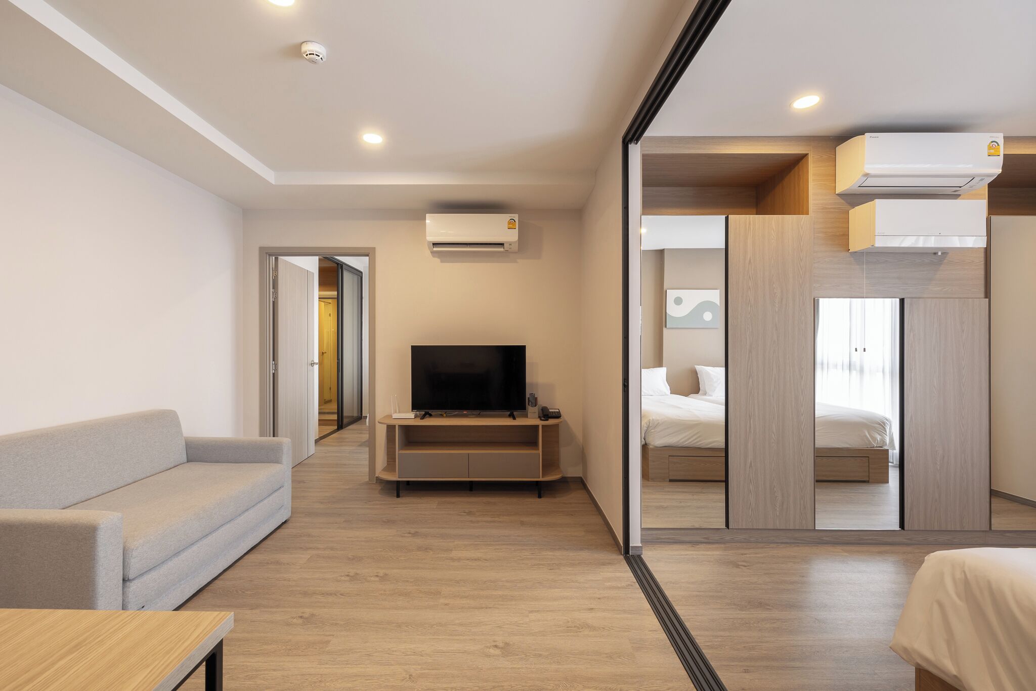 Une chambre d’hôtel moderne dotée d’une télévision à écran plat, d’un canapé, d’un parquet et d’un lit avec une tête de lit en bois.