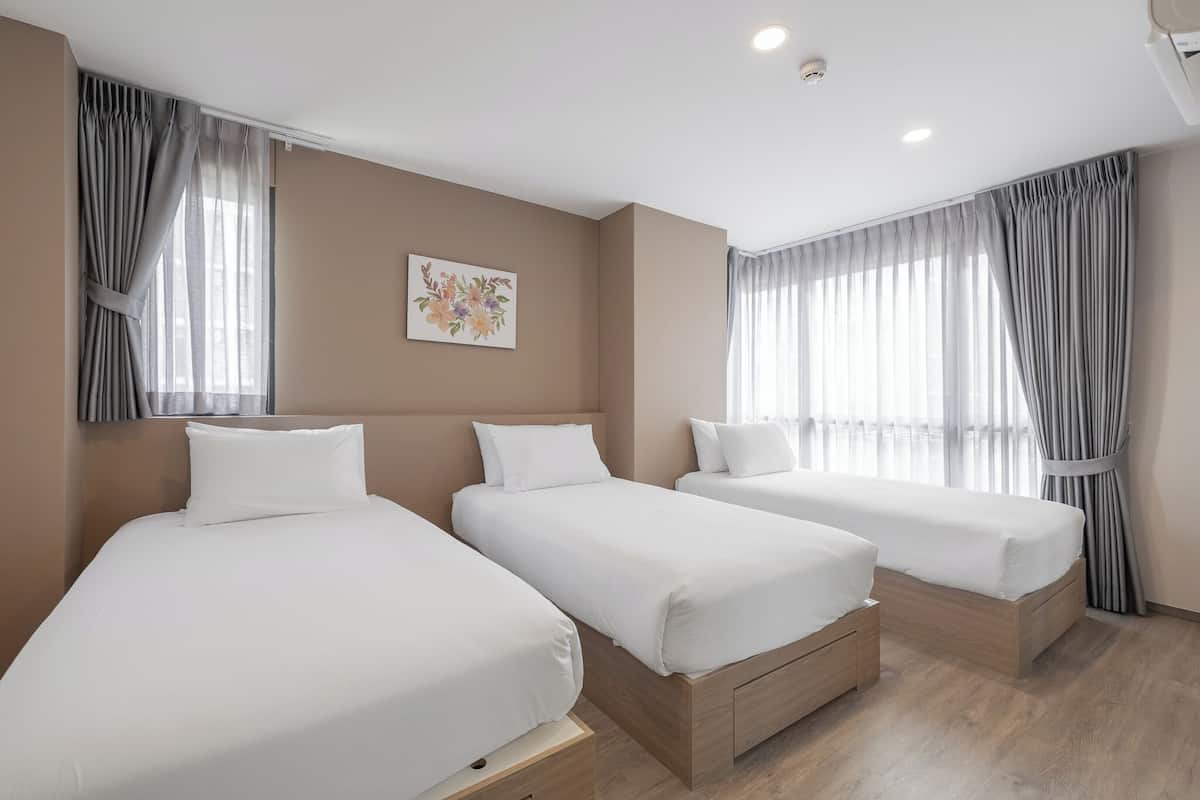 Ein Hotelzimmer mit drei Einzelbetten, einer Deckenleuchte, einem Wandbild und großen Fenstern mit Vorhängen.