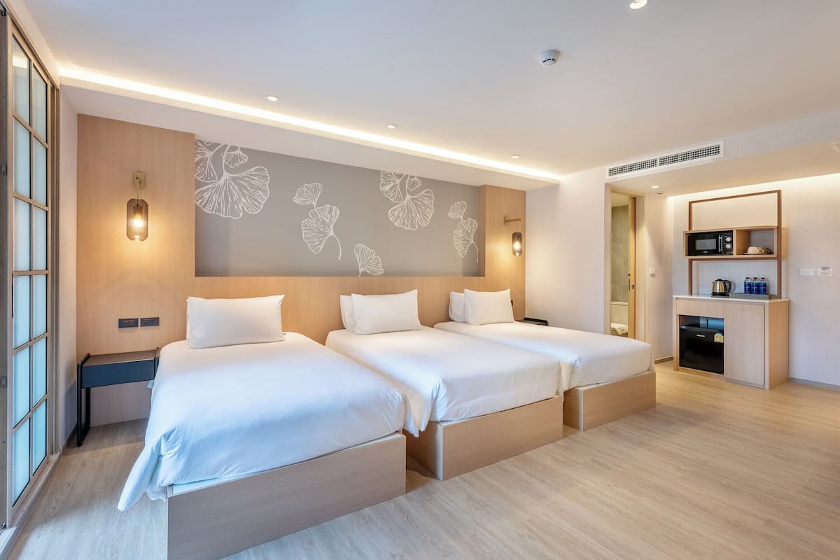 Ein modernes Hotelzimmer mit zwei Betten, einer Holzvertäfelung, Wandbild mit Blättern, integriertem Schreibtisch und einer Küchenzeile.