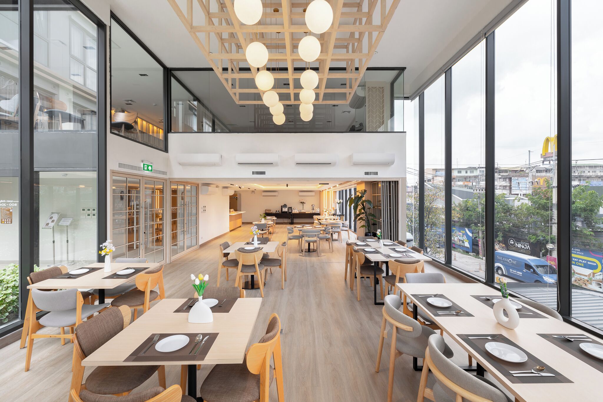 Un comedor moderno con mesas largas, sillas y un techo alto con luces colgantes.