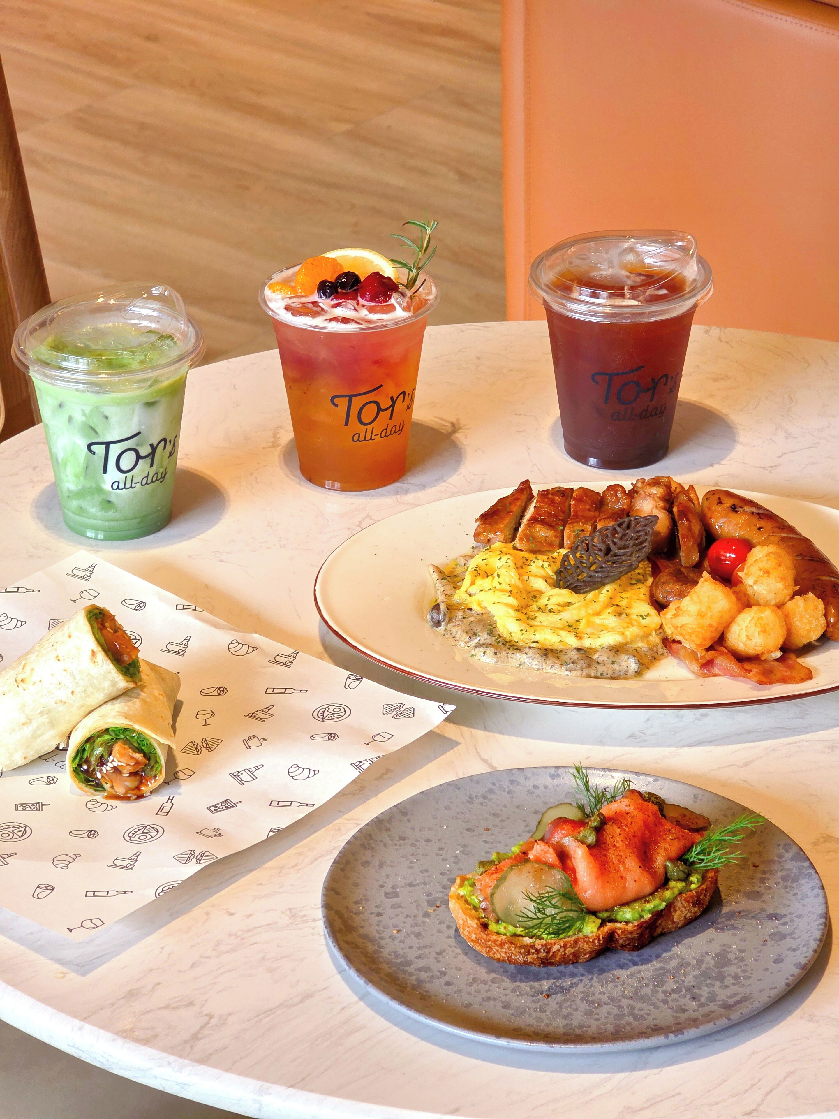 A table with various food items including a wrap, a plate of eggs, and two drinks.