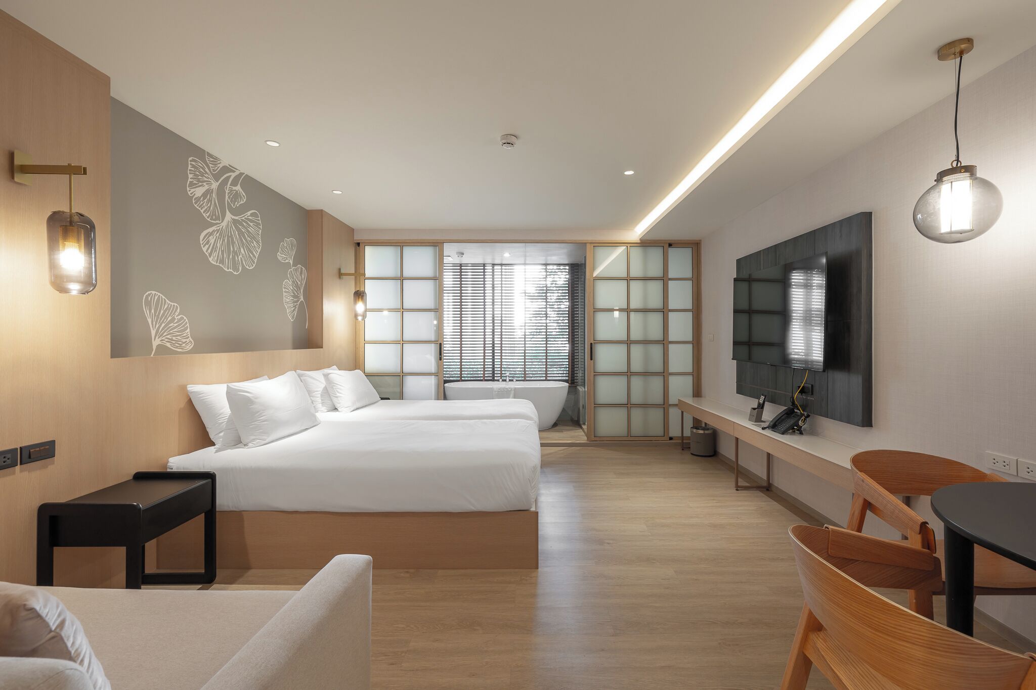 A modern hotel room with a large bed, a desk, a TV, and a view of the outside through large windows.