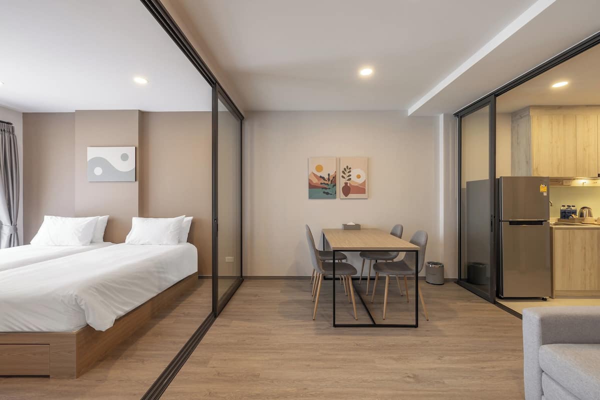 Ein modernes Hotelzimmer mit einem Bett, einem Esstisch mit Stühlen, einer Küchenzeile und Bildern an der Wand.