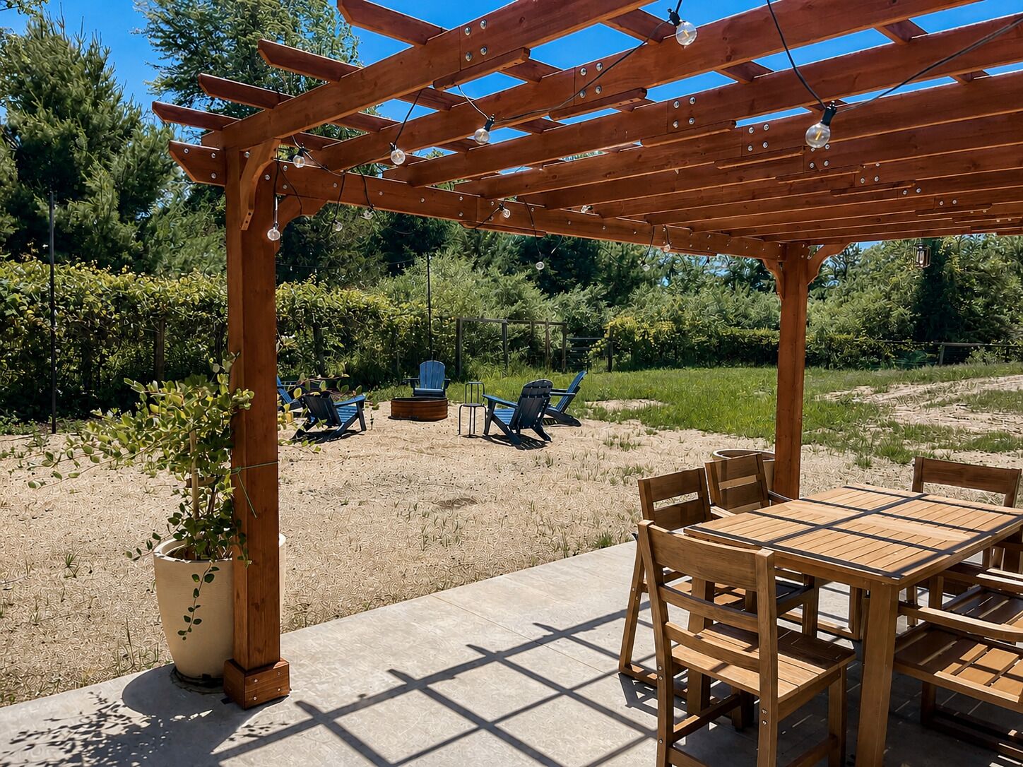 Eine Holz-Pergola mit Lichterketten, einem Terrassentisch und blauen Stühlen in einem Garten.
