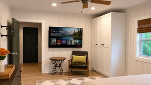 Ein Schlafzimmer mit Bett, Sessel, Tisch, Fernseher und Kleiderschrank.