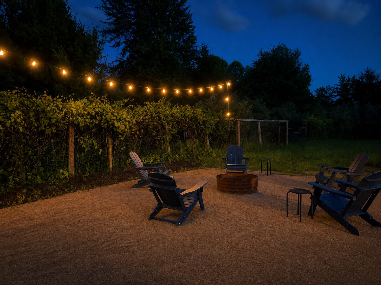 An outdoor seating area with Adirondack chairs, a fire pit, and string lights.