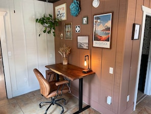 Un bureau en bois avec une chaise, une plante suspendue, un tableau encadré représentant Saugatuck, dans le Michigan, et une lampe fixée au mur.