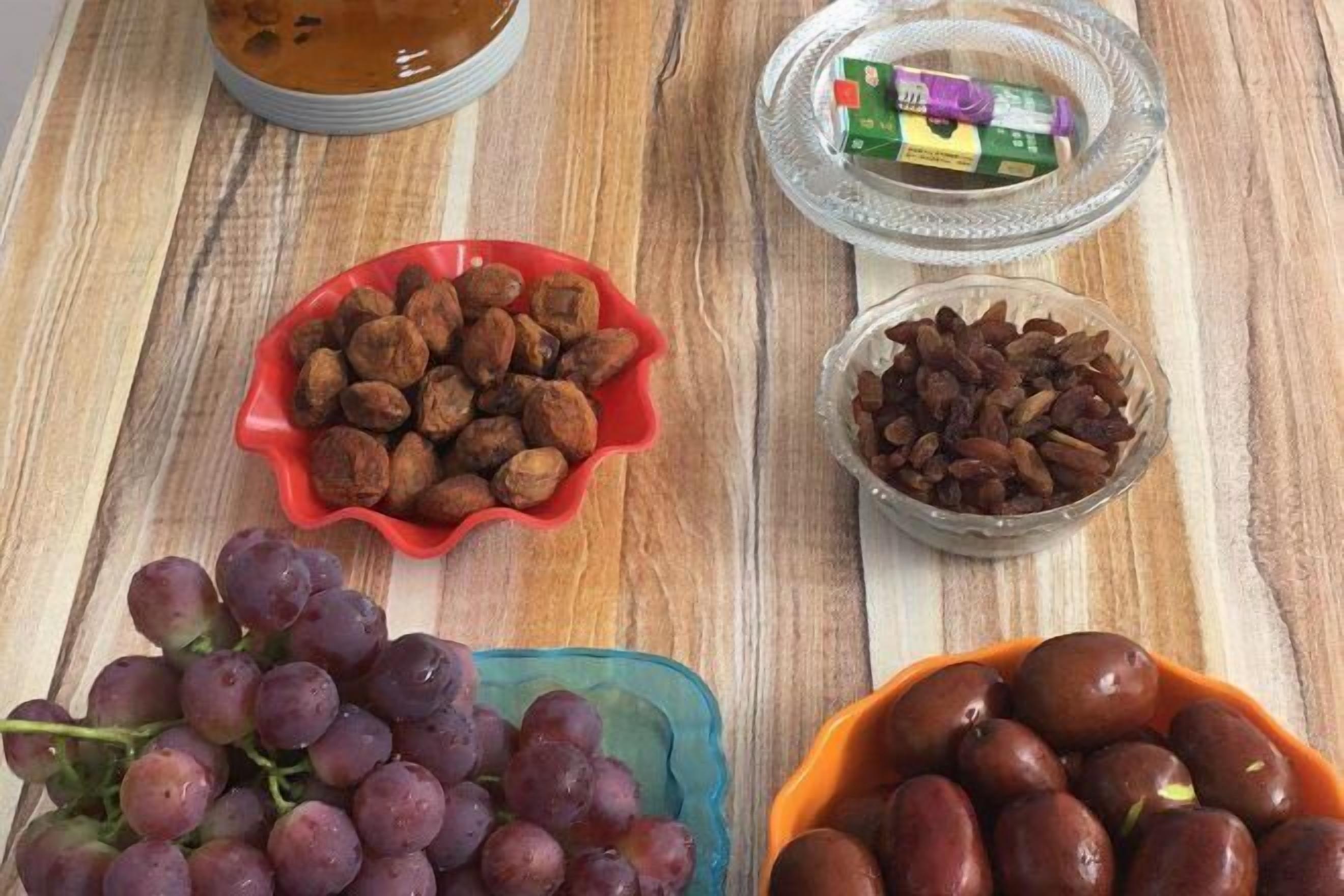 Uma mesa de madeira com tigelas de uvas, nozes e frutas secas.