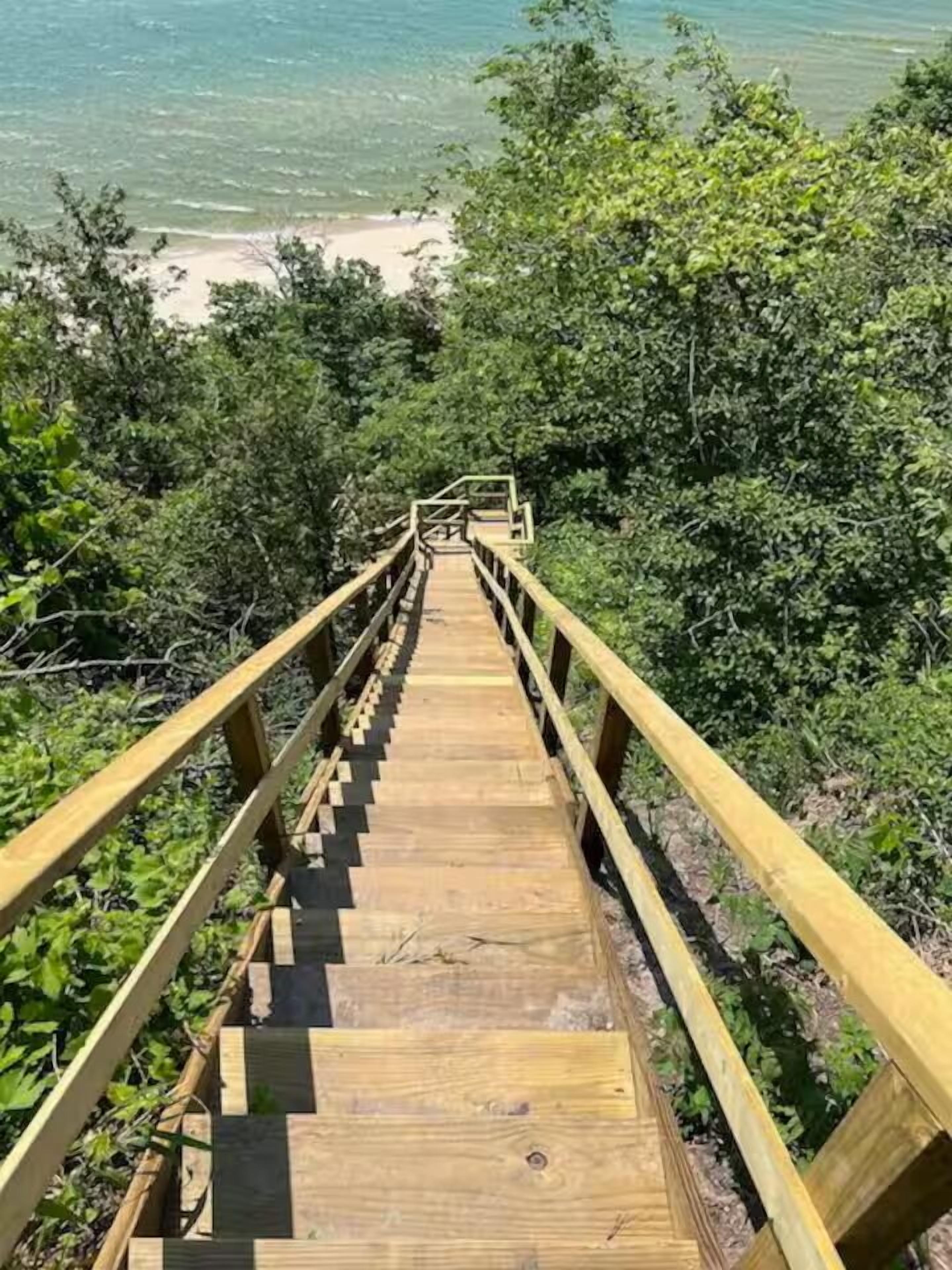 Eine Holztreppe führt zu einem Strand, umgeben von üppigem Grün.