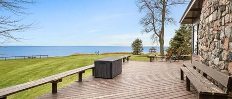 A wooden deck with benches and a trash bin overlooking a grassy area and a body of water.