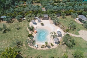 Vue aérienne d’une propriété aménagée avec une piscine, des chaises longues et un petit bâtiment.