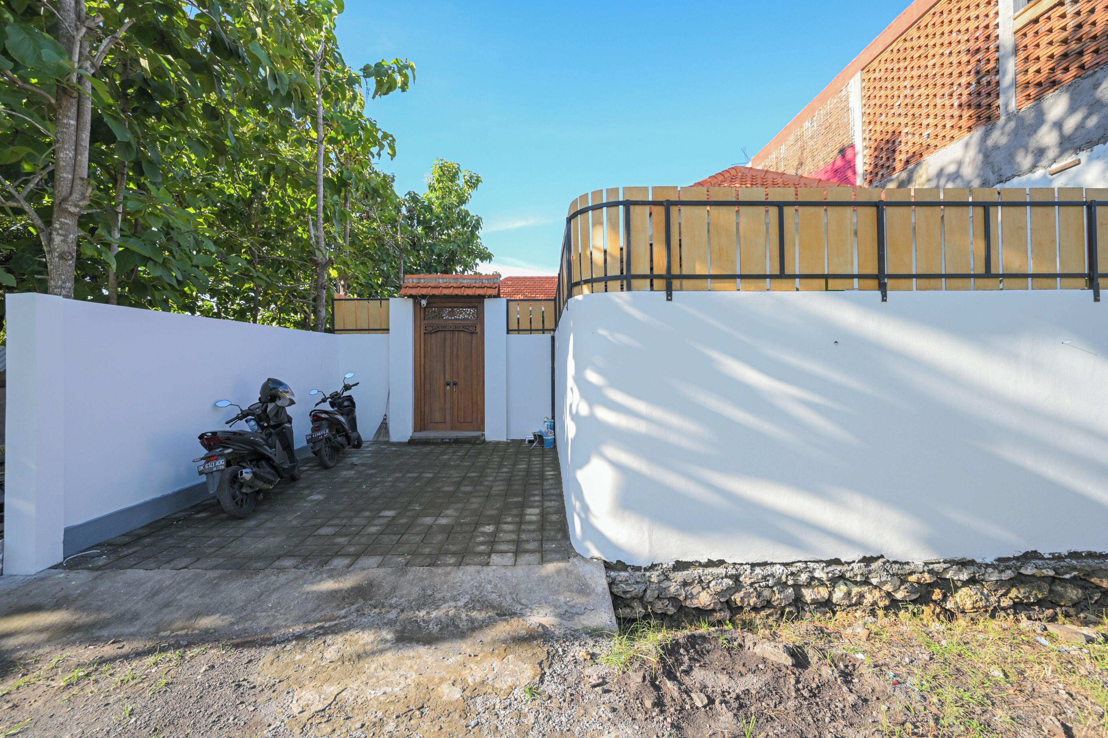 A paved driveway leading to a gated entrance with a white wall and a wooden fence.