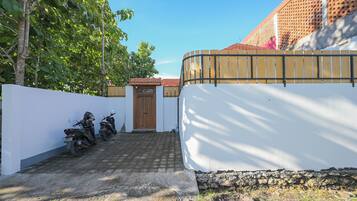 A paved driveway leading to a gated entrance with a white wall and a wooden fence.