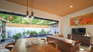 A spacious dining area with a wooden table and chairs, a television, and a large window overlooking a garden.