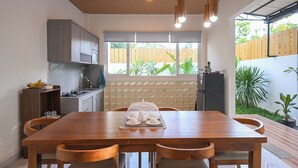 A modern kitchen with a dining area, wooden cabinets, a window with a view of greenery, and pendant lighting.