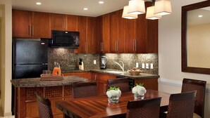 Una cocina moderna con armarios de madera, un refrigerador negro, un microondas, encimeras de granito y un comedor con mesa y sillas de madera.