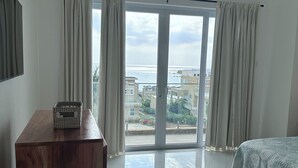 A bedroom with a large sliding glass door leading to a balcony, a wooden dresser, and a bed with a patterned bedspread. - OneLoveVilla is a charming ocean view beach house in New Hope, Westmoreland JA (New Hope)