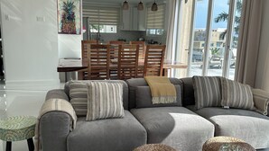 A modern living room with a grey sectional sofa, a wooden coffee table, and a dining area with a wooden table and chairs. - OneLoveVilla is a charming ocean view beach house in New Hope, Westmoreland JA (New Hope)