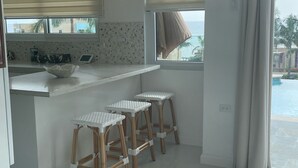 A modern kitchen with three hanging pendant lights, a white countertop, and a window with blinds. - OneLoveVilla is a charming ocean view beach house in New Hope, Westmoreland JA (New Hope)