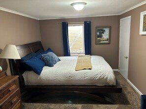 A bedroom with a bed, a dresser, a window with curtains, a door, and a ceiling light. - 3-bedroom House in Rapid City for Sturgis Rally with Two Car Garage for Bikes (Rapid City)