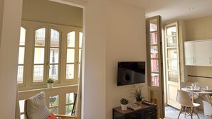 A room with a large window, a television, a dining table with chairs, and a cabinet. - EL BALCÓN MÁLAGA MALAGA (MALAGA)